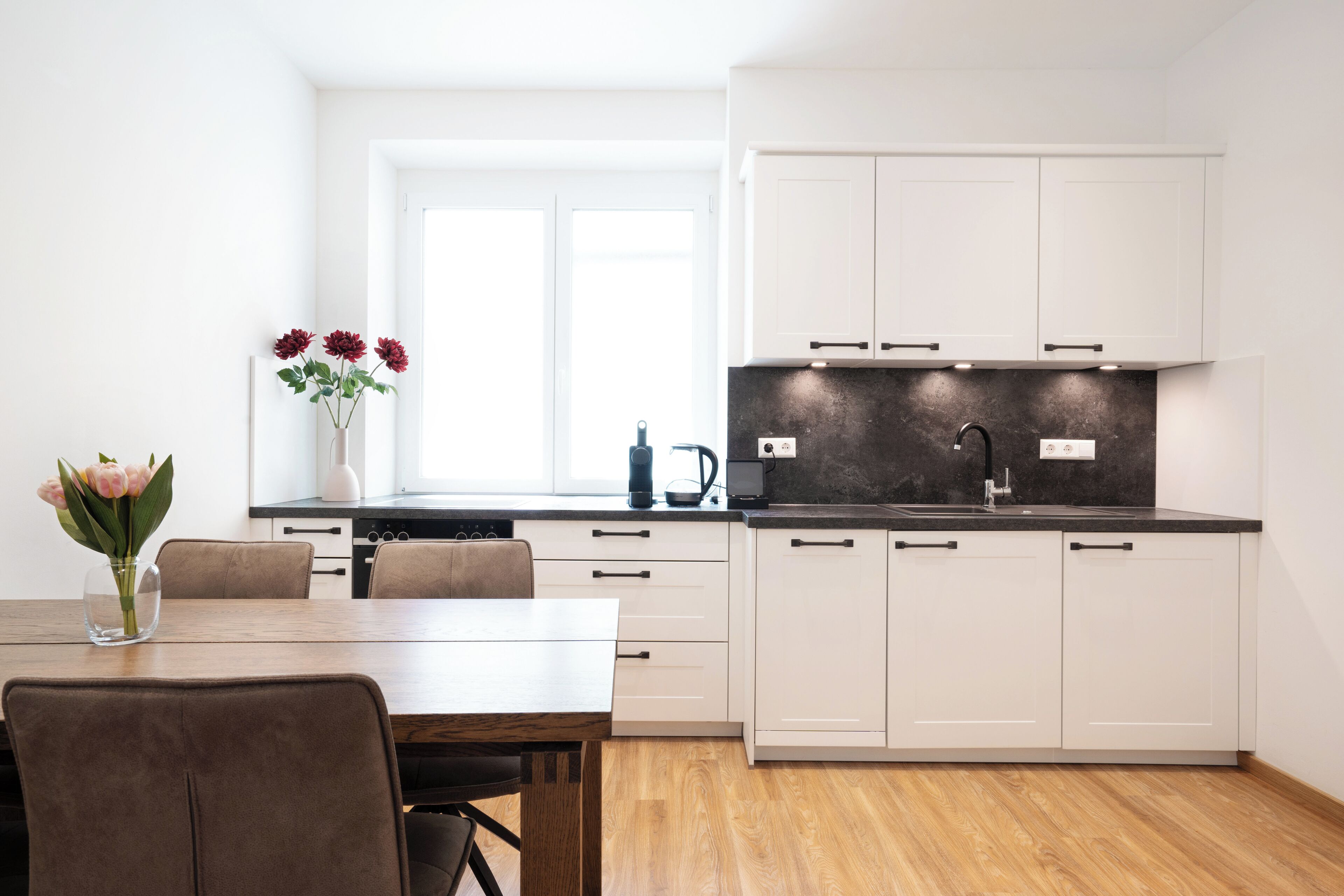 A modern kitchen with white cabinets, a black countertop, and a window above the sink.
