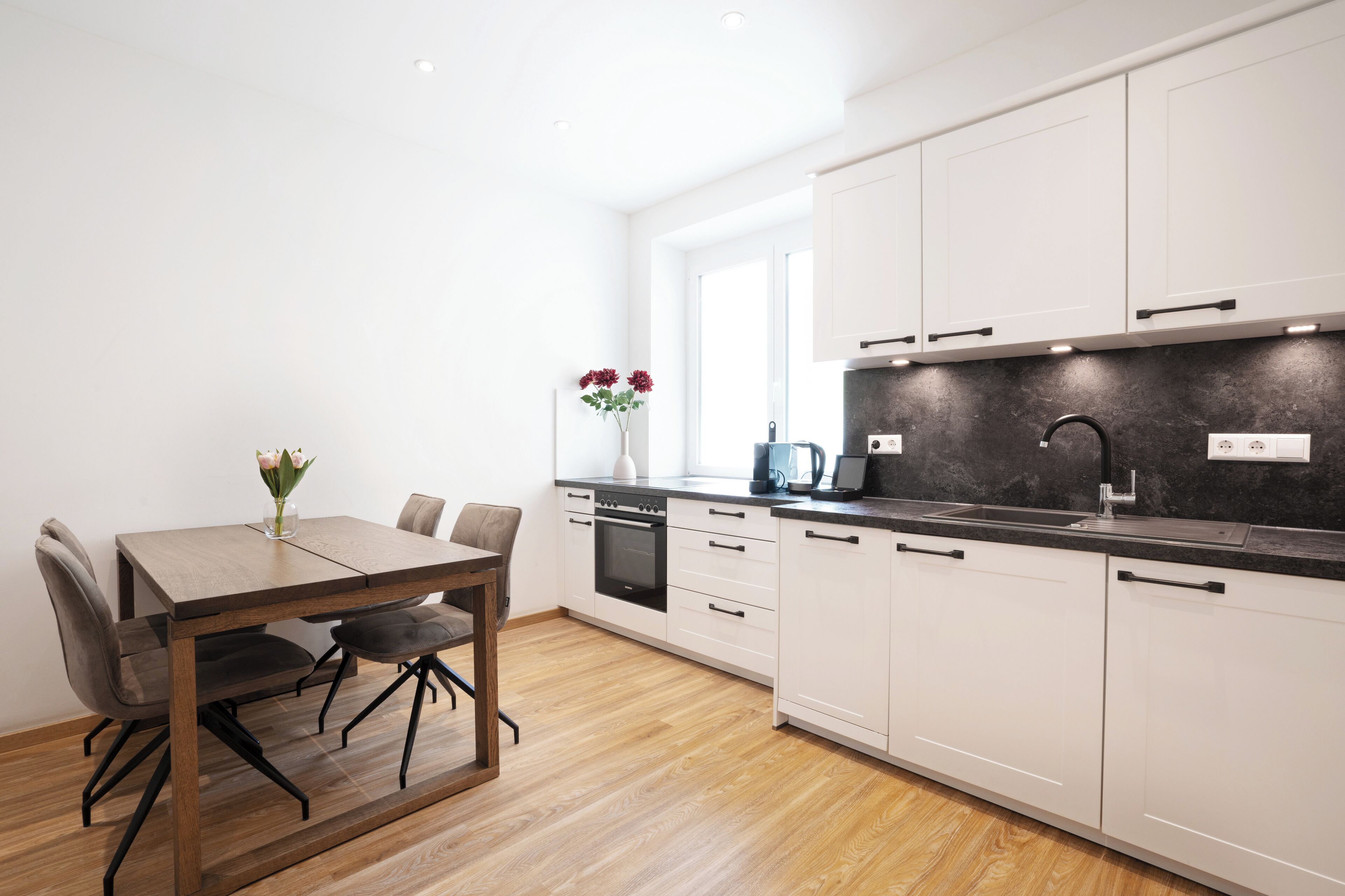 Een moderne keuken met witte kasten, een houten eettafel en een zwart aanrecht.