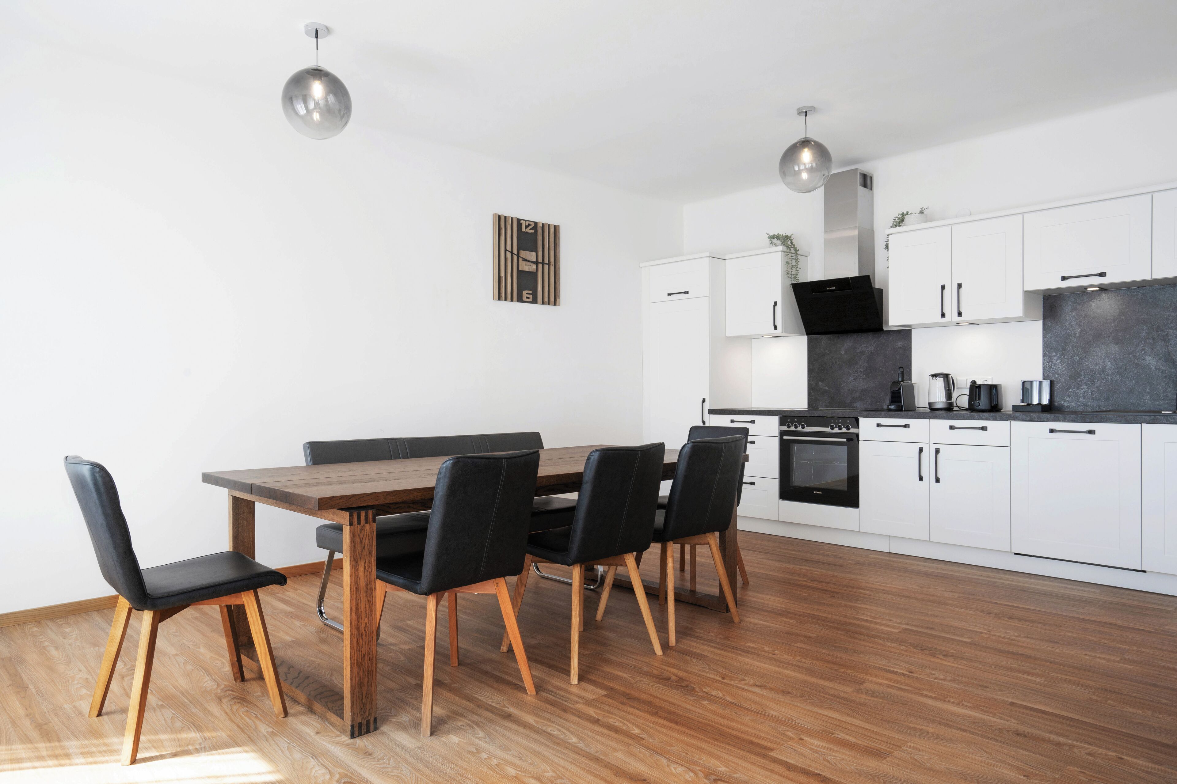 A modern kitchen with white cabinets, a wooden dining table, and black chairs.