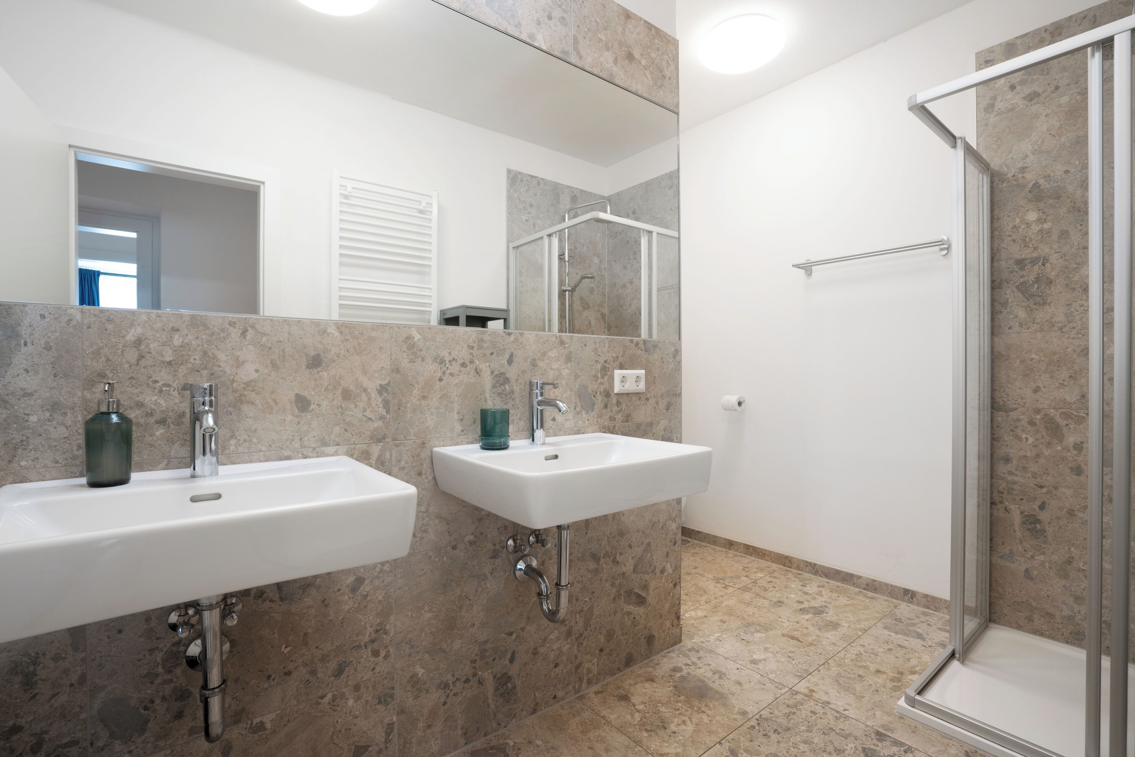 A modern bathroom with two sinks, a shower, and a large mirror.