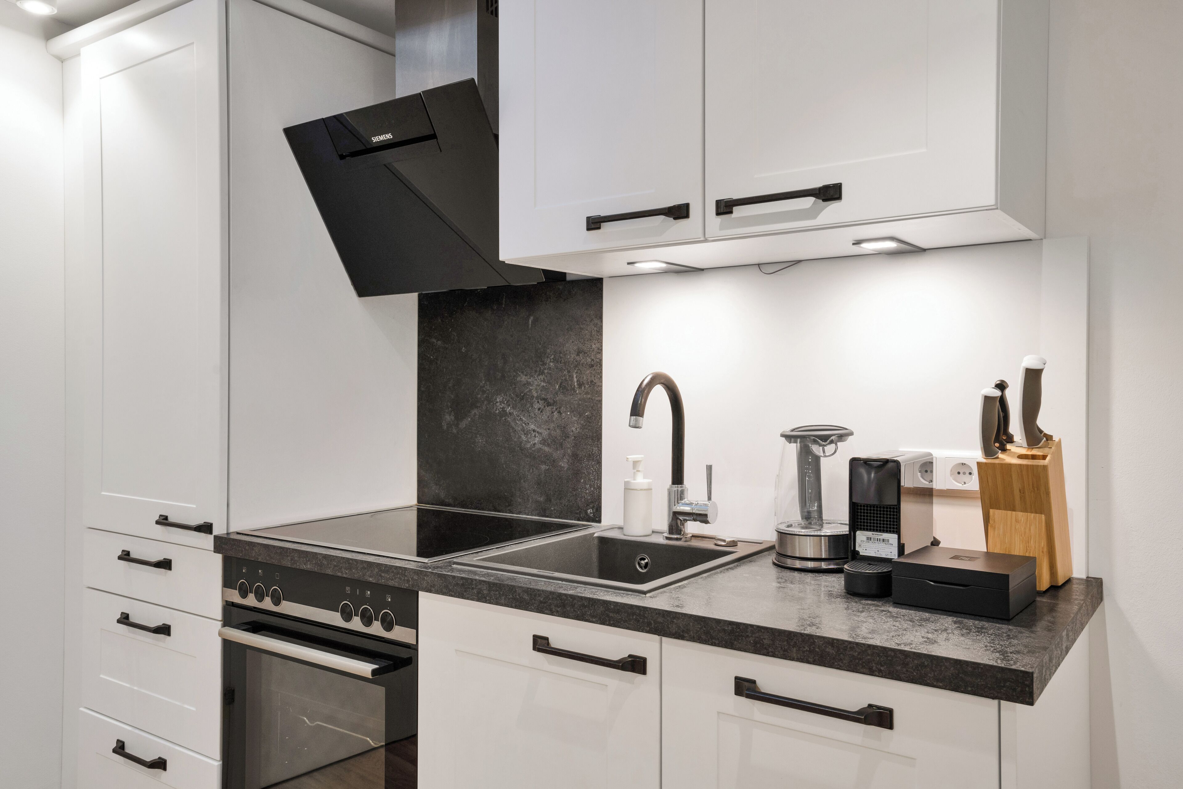 Una cocina moderna con armarios blancos, encimera negra y electrodomésticos de acero inoxidable.
