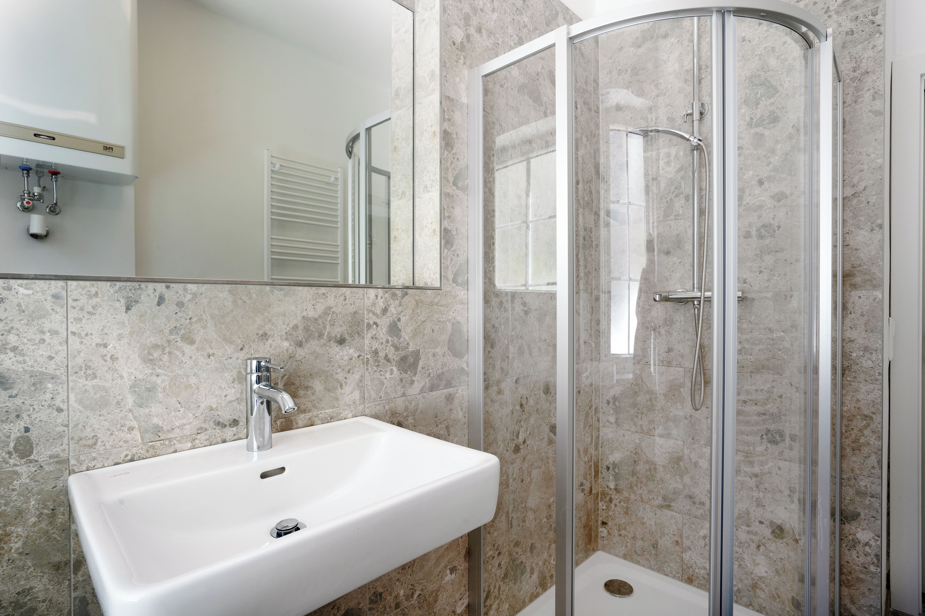 A bathroom with a white sink, a glass shower enclosure, and a marble-tiled wall.