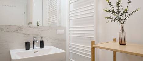 A bathroom with a white sink, two black bottles, a mirror, and a wooden shelf with a vase of green plants.
