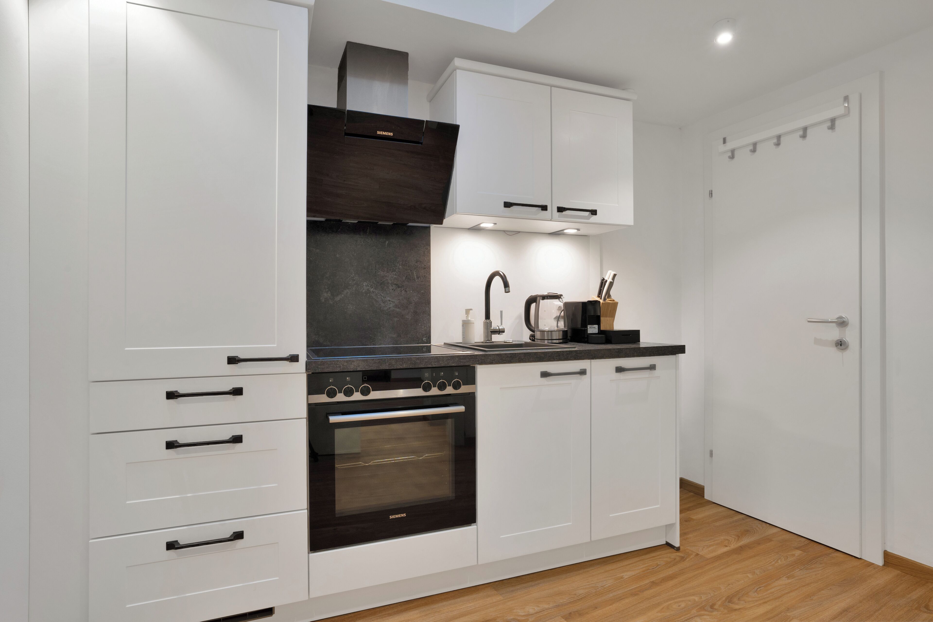 A modern kitchen with white cabinetry, a built-in oven, and a stainless steel range hood.