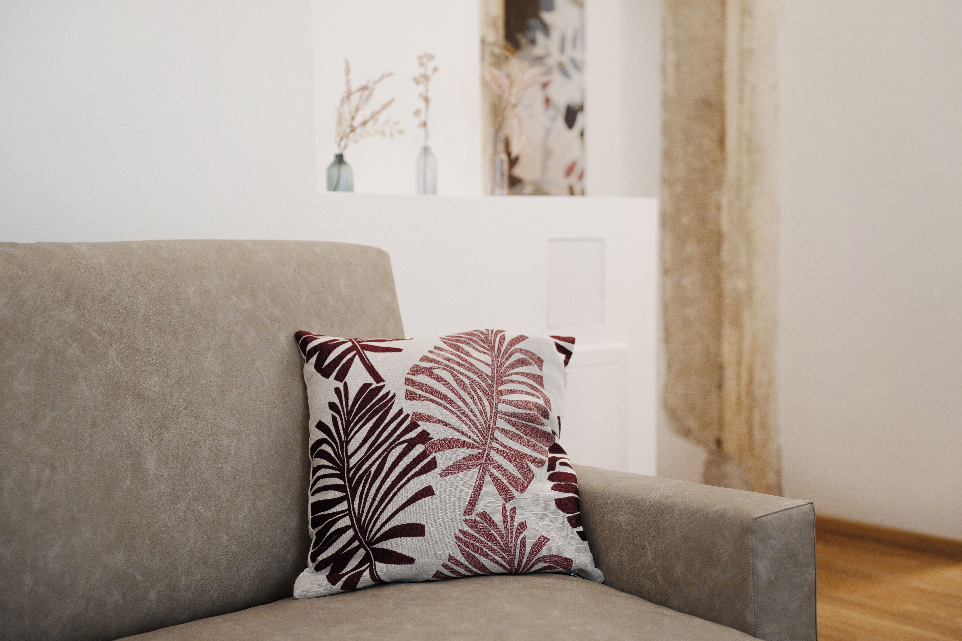 Una poltrona dai toni neutri con un cuscino decorato, una porta bianca e un muro con arte astratta e piante essiccate.