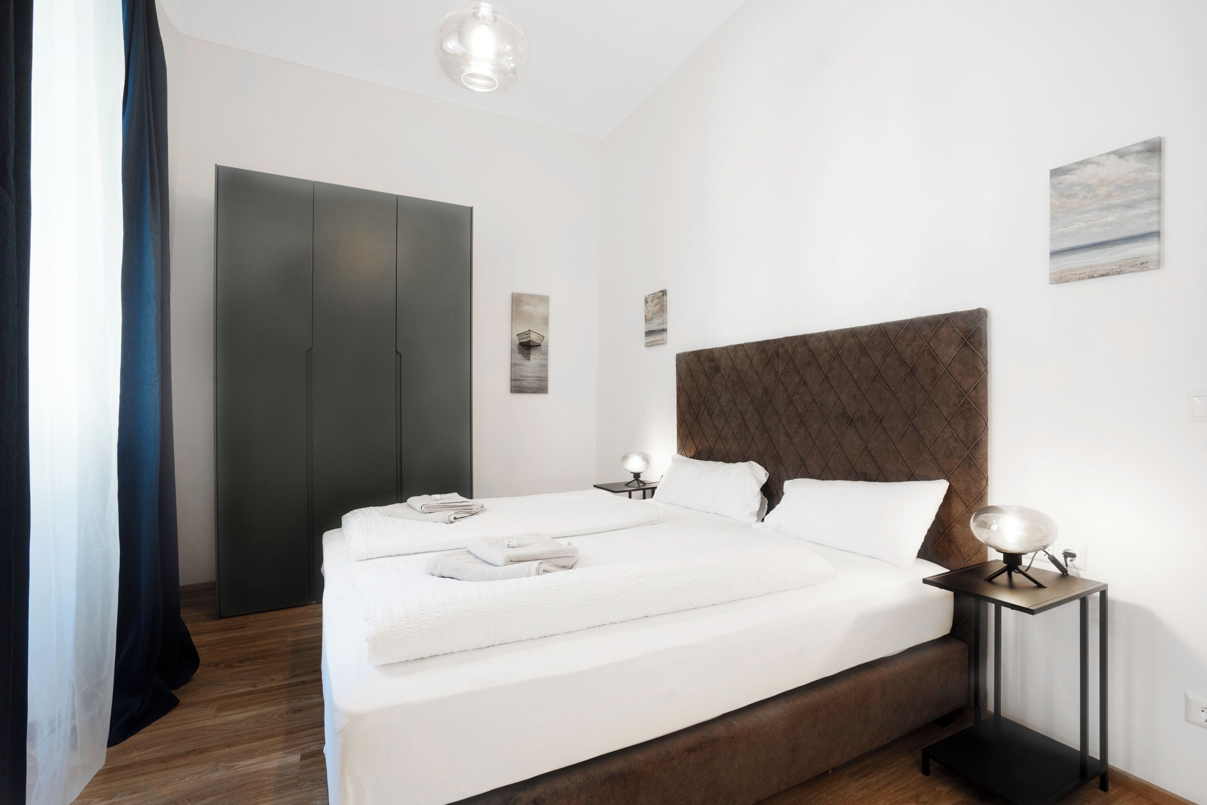 A modern bedroom with a large bed, bedside tables, and a wardrobe.