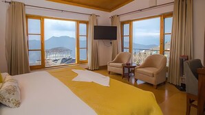A hotel room with a large bed, two armchairs, a TV, and a balcony with a mountain view. - aMALA Villa - Six Bedroom Luxurious Villa with Himalayan View (Kaudia Range)