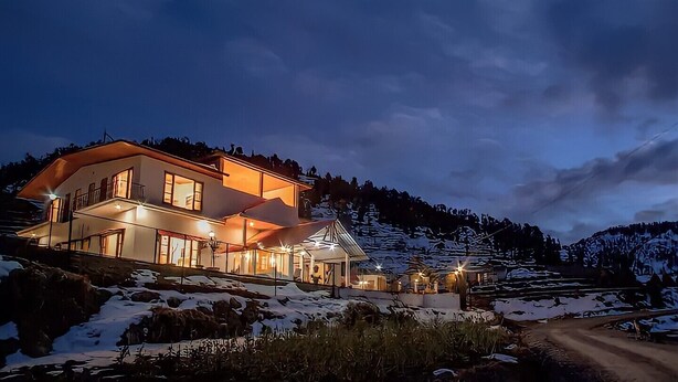 A two-story house with multiple windows and a balcony, surrounded by snow-covered hills. - aMALA Villa - Six Bedroom Luxurious Villa with Himalayan View (Kaudia Range)