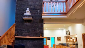 A spacious living area with a high ceiling, a stone accent wall, a chandelier, and a staircase leading to an upper level. - aMALA Villa - Six Bedroom Luxurious Villa with Himalayan View (Kaudia Range)