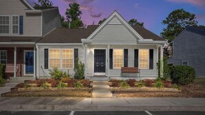 A two-story house with a front porch, a small front yard with plants, and a driveway.