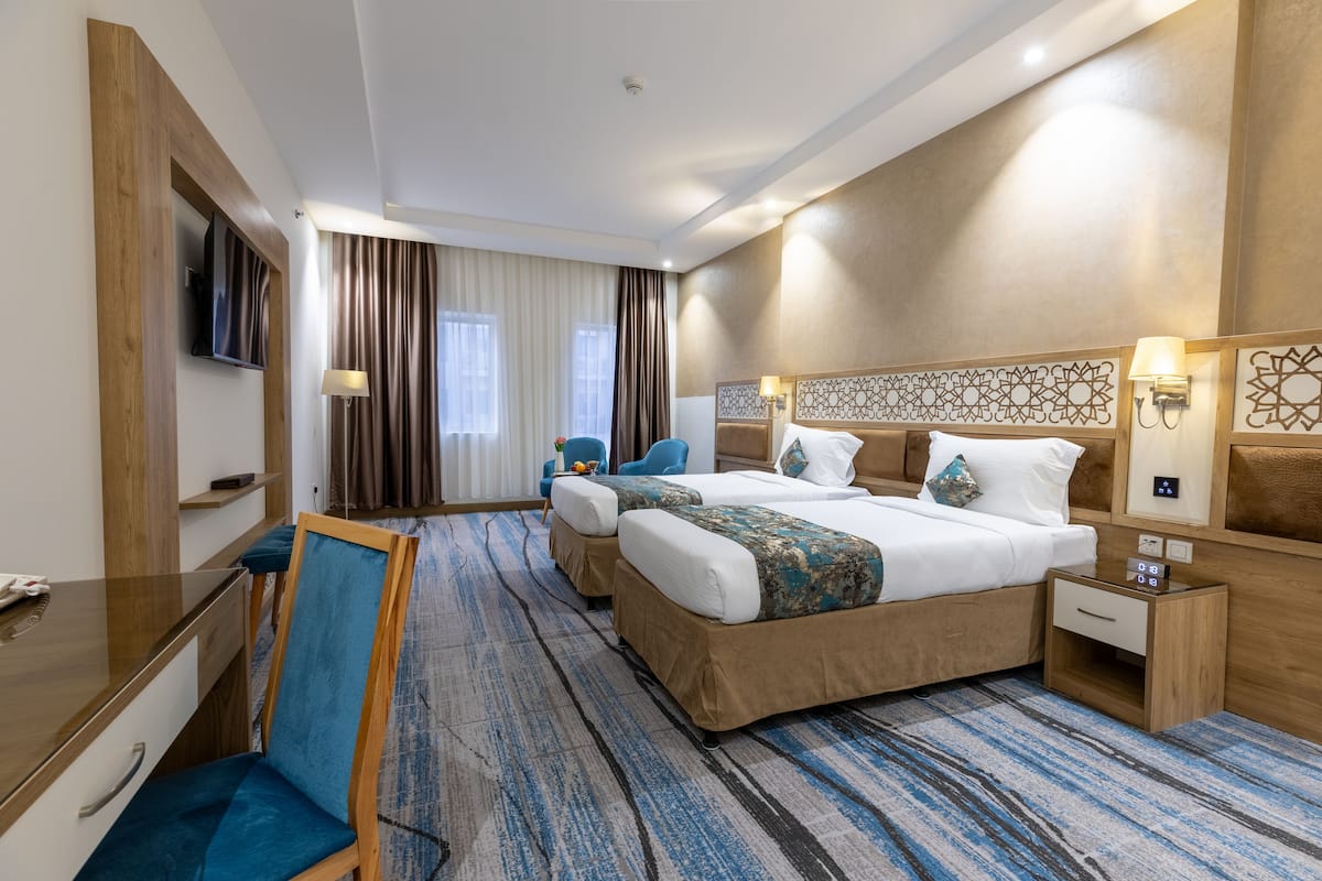 A hotel room with a large bed, a desk, a chair, a TV, and a nightstand.