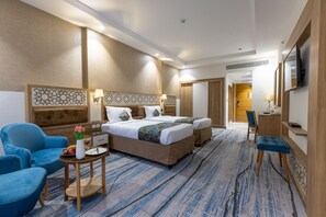 A hotel room with a large bed, two blue armchairs, a small table with a vase of flowers, and a TV mounted on the wall. - TIME Ruba Hotel & Suites (Makkah)