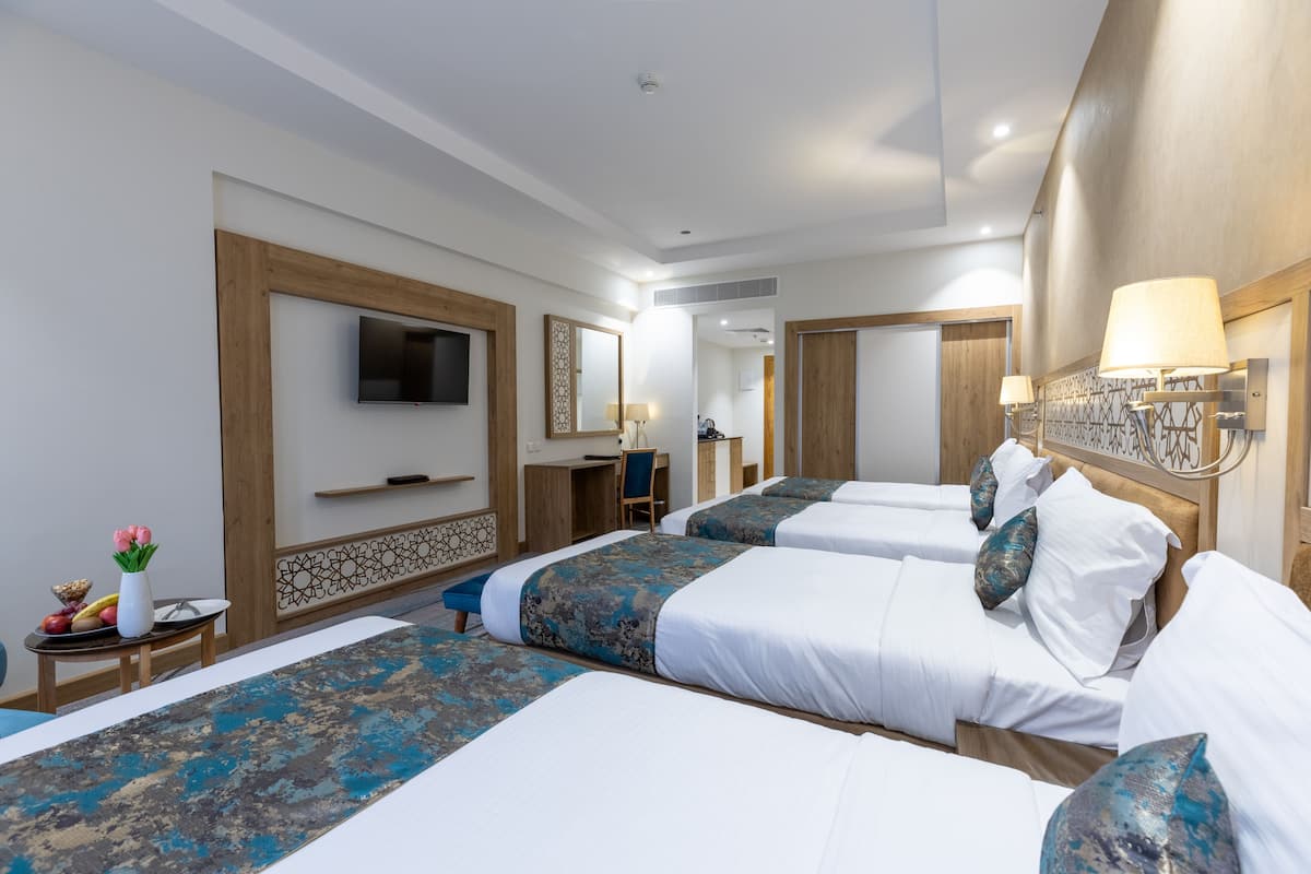 A hotel room with four beds, a desk, a TV, and a bathroom visible through an open door.