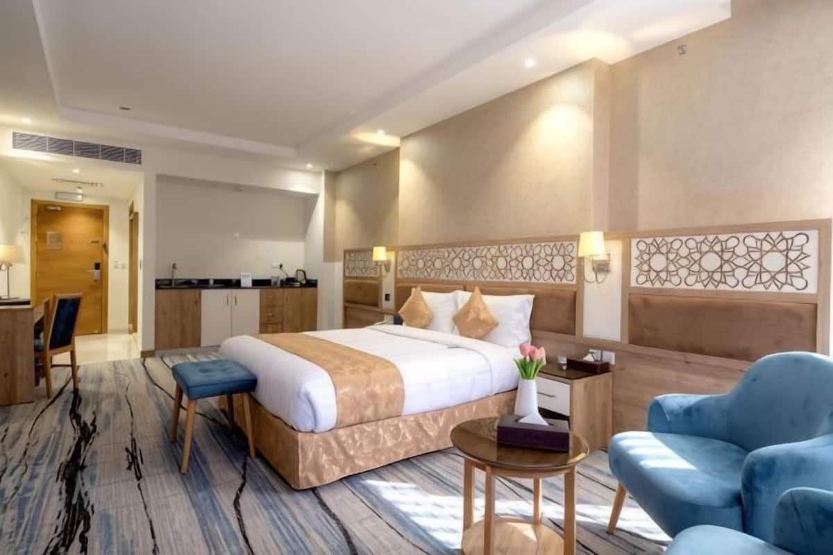 A hotel room with a large bed, a desk, a chair, and a small table with a vase.