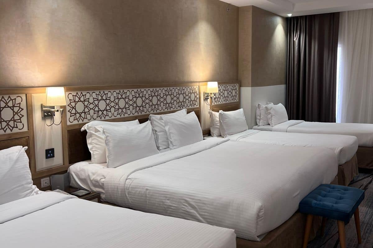 A hotel room with three beds, a large window with curtains, and a patterned headboard.