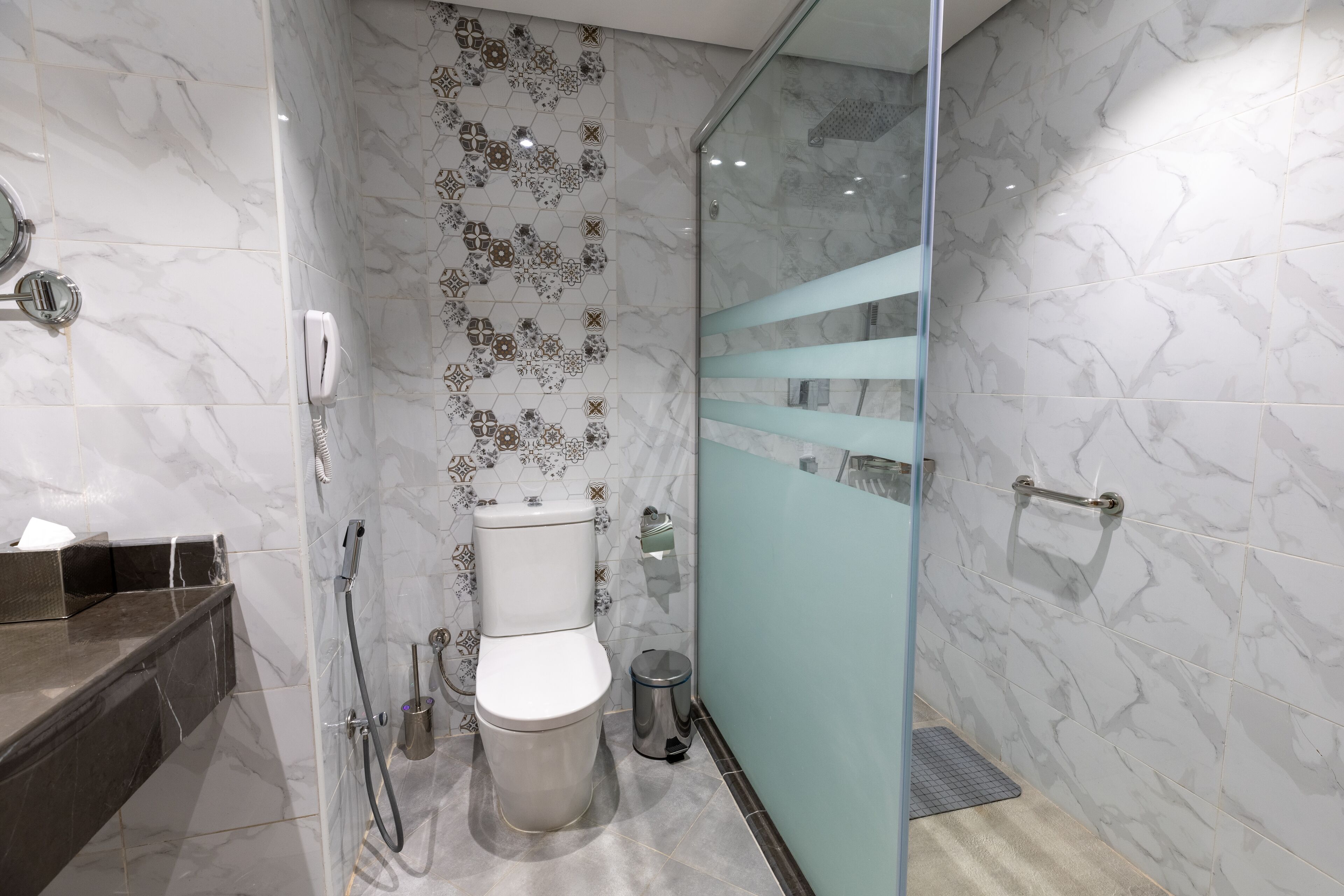 A modern bathroom with a glass shower enclosure, a toilet, and a trash can.