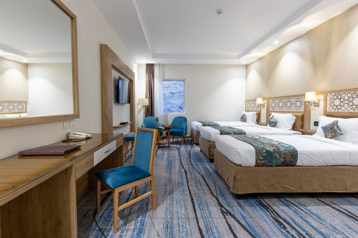 A hotel room with a desk, two beds, a chair, a TV, and a window.
