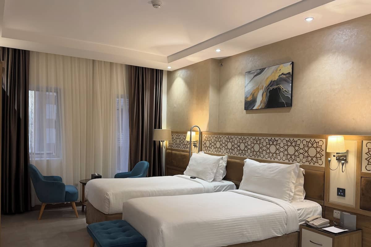A hotel room with two beds, a desk, a chair, and a large window with curtains.