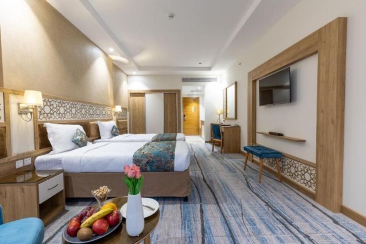 A hotel room with two beds, a desk, a TV, and a fruit bowl on the side table.