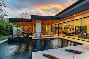 A modern house with a swimming pool, outdoor seating, and a large glass window.