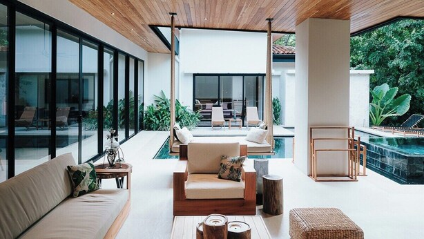 A modern living room with a wooden ceiling, large windows, a pool, and outdoor seating. - Avara House (Reserva de Golf, Hacienda Pinilla)