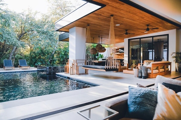 A modern outdoor living area with a pool, seating, and a wooden ceiling.