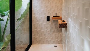 A modern bathroom with a wooden ceiling, a textured wall, a sink, and a large window with a view of greenery. - Avara House (Reserva de Golf, Hacienda Pinilla)