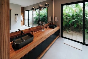 A modern bathroom with a wooden vanity, black sink, and a large mirror.