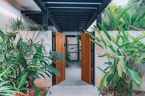 A pathway leading to a room with a modern design, featuring a concrete floor and a wooden door frame.