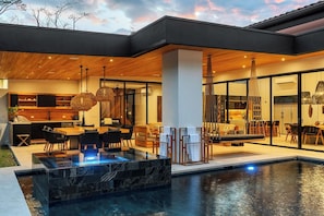 A modern house with a swimming pool, outdoor seating, and a kitchen area.