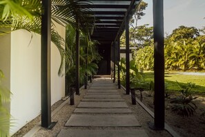 A covered walkway with a gravel path, surrounded by greenery and palm trees.