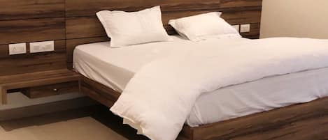 A bed with a wooden headboard, white bedding, and a bedside table with a drawer.