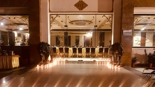 Un vestíbulo de hotel con una recepción, una araña y una fila de mesas y sillas.