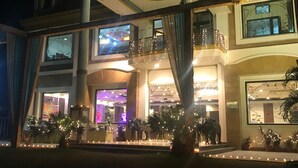Un hotel de varios pisos con una entrada imponente, ventanas amplias y un balcón con luces colgantes.