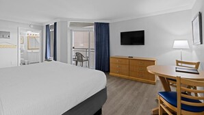 Ein Hotelzimmer mit einem großen Bett, einem Holzschrank, einem runden Tisch mit Stühlen, einem an der Wand montierten Fernseher und einem Balkon mit einem Stuhl.