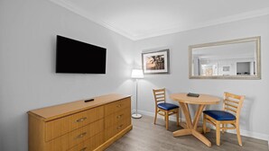 Ein Zimmer mit einem Holzkapständer, einem Flachbildfernseher, einer Lampe, zwei Stühlen und einem runden Tisch.