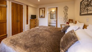 Een slaapkamer met een groot bed, een houten garderobe, een televisie op een houten kast en een zichtbare badkamer door een geopende deur.