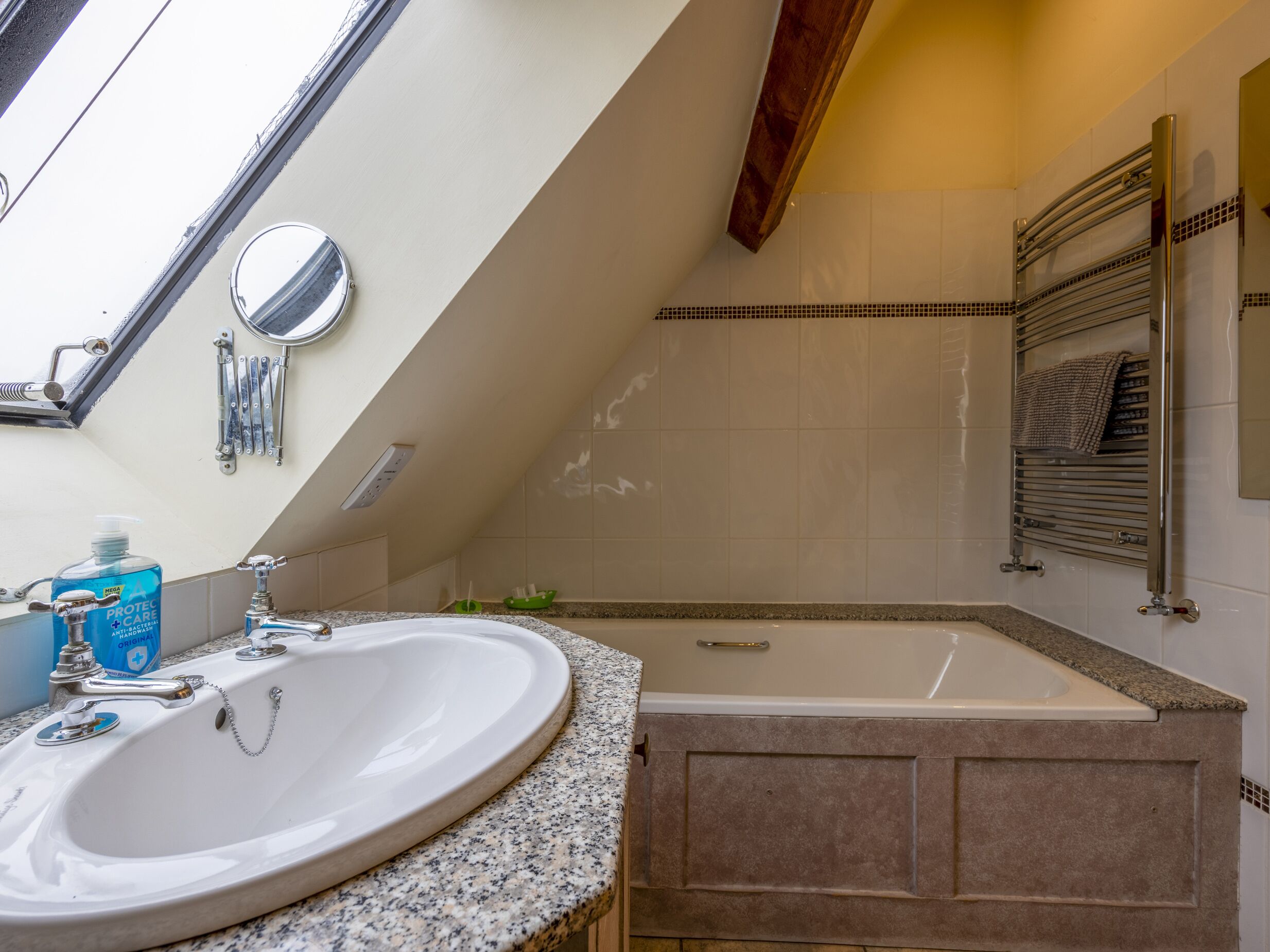 A bathroom with a freestanding bathtub, a sink with a granite countertop, and a skylight above.