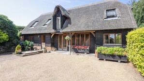 Een rustiek houten huis met rieten dak, houten balken en een grindpad.