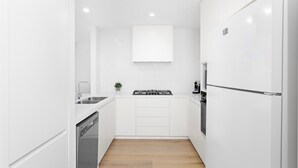 A compact kitchen with white cabinetry, a gas stove, a dishwasher, and a refrigerator. - Wine Down - Small family getaway (Kiama)