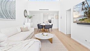 A modern living room with a white sofa, a round coffee table, and a dining area with a white table and chairs. - Wine Down - Small family getaway (Kiama)