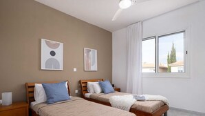 Ein Schlafzimmer mit zwei hölzernen Betten, einem Nachttisch, einem Deckenventilator und einem Fenster mit Vorhängen.