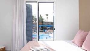 Ein Schlafzimmer mit Bett, Fenster und Blick auf einen Pool und Palmen.