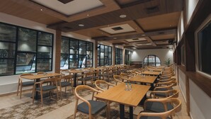 Un comedor espacioso con varias mesas y sillas de madera, ventanas amplias que ofrecen vistas, y un diseño moderno de techo.