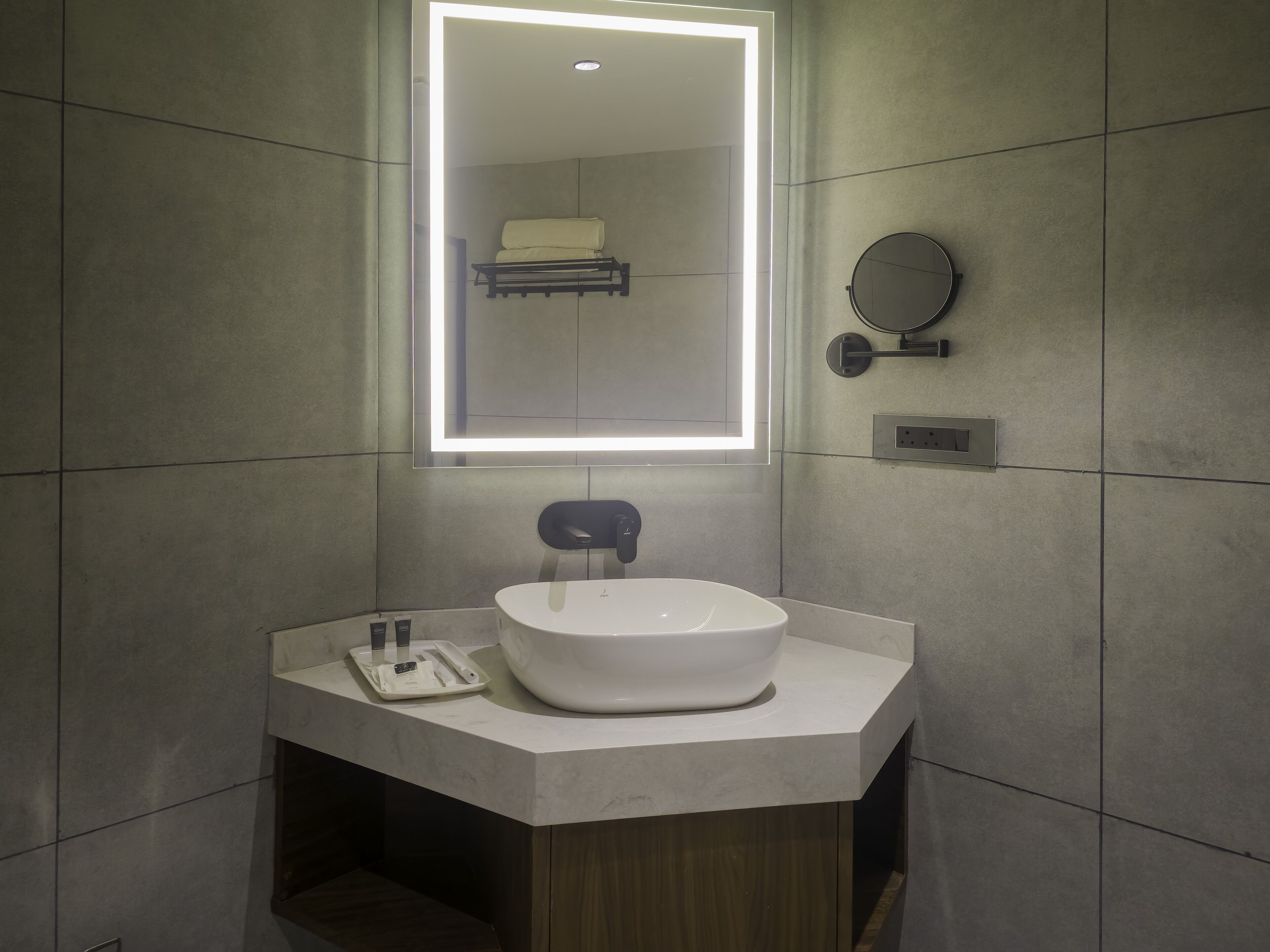 A modern bathroom with a large mirror, a white sink, and a towel rack.
