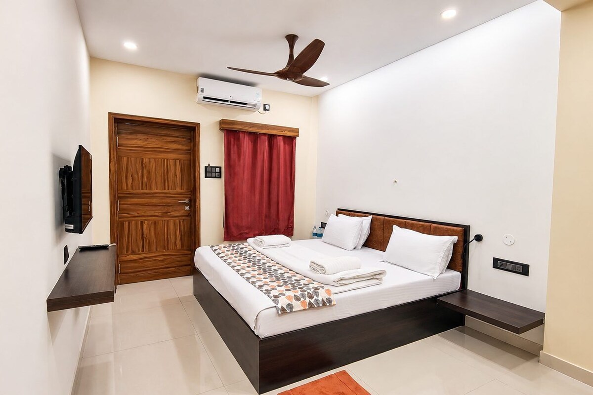 A bedroom with a bed, a TV, a ceiling fan, and a door.