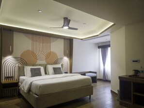 A modern hotel room with a large bed, a ceiling fan, and a desk with a chair.