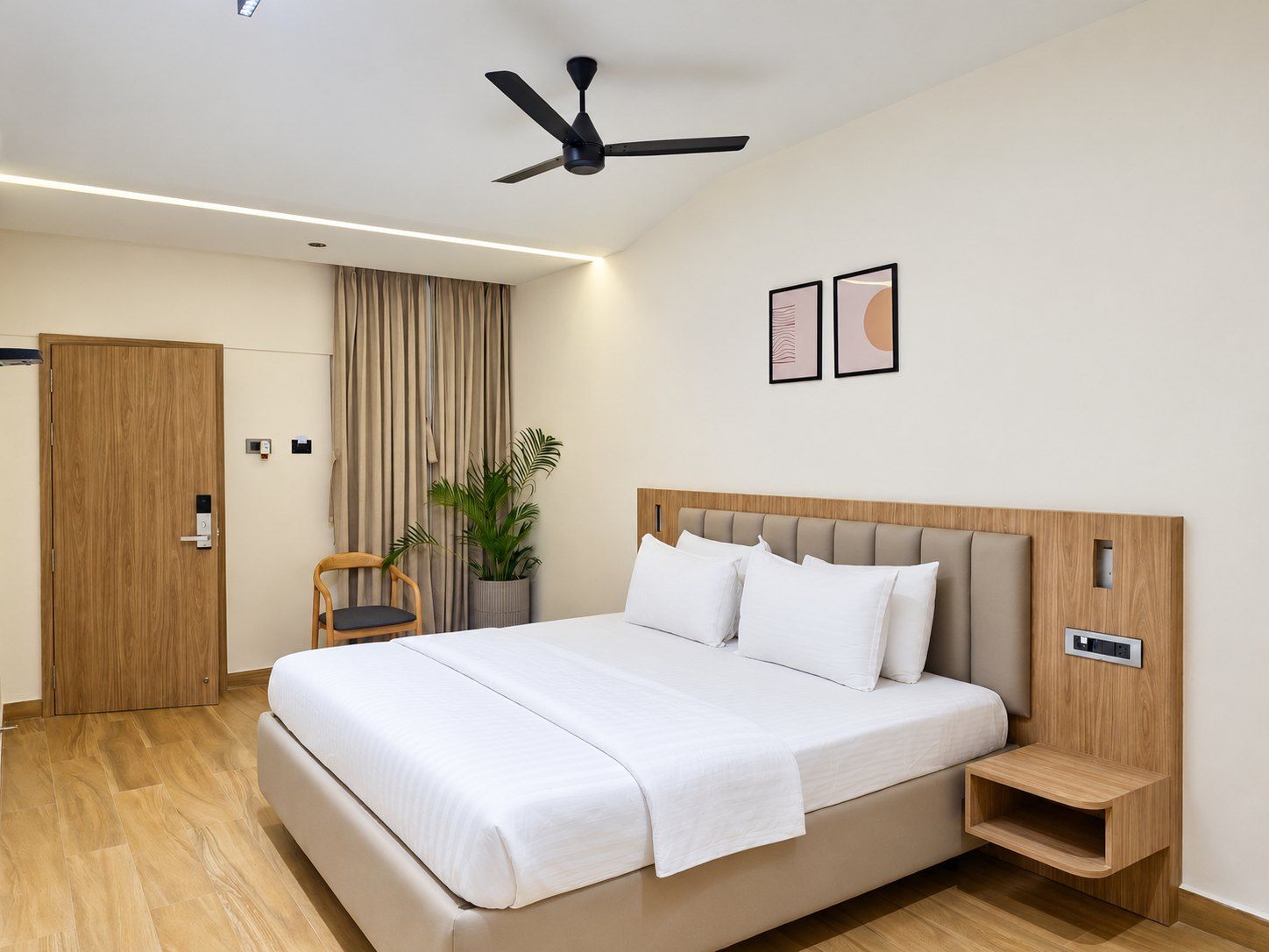 A modern hotel room with a large bed, a ceiling fan, a potted plant, and a wooden nightstand.