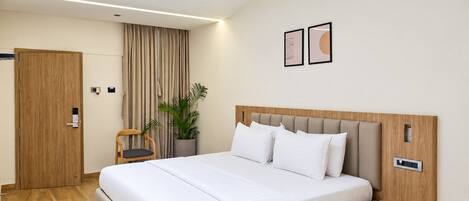 A modern hotel room with a large bed, a ceiling fan, a potted plant, and a wooden nightstand.