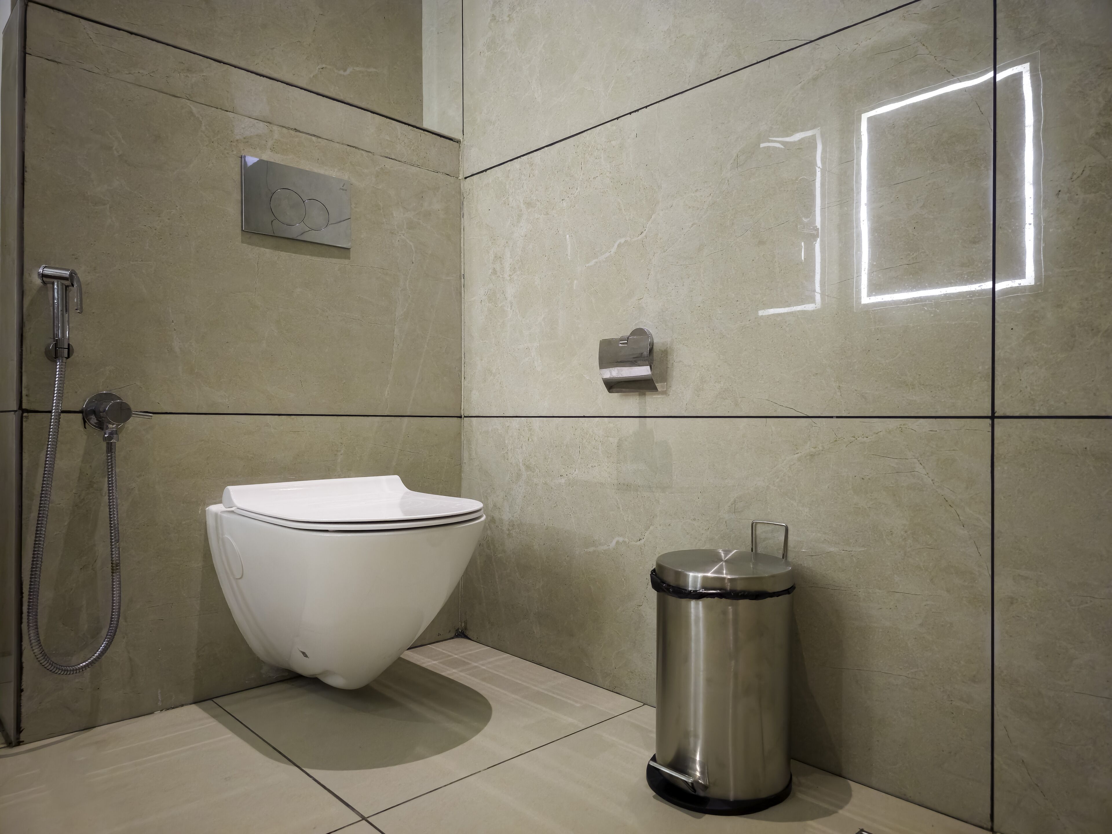A modern bathroom with a toilet, a shower, and a trash bin.